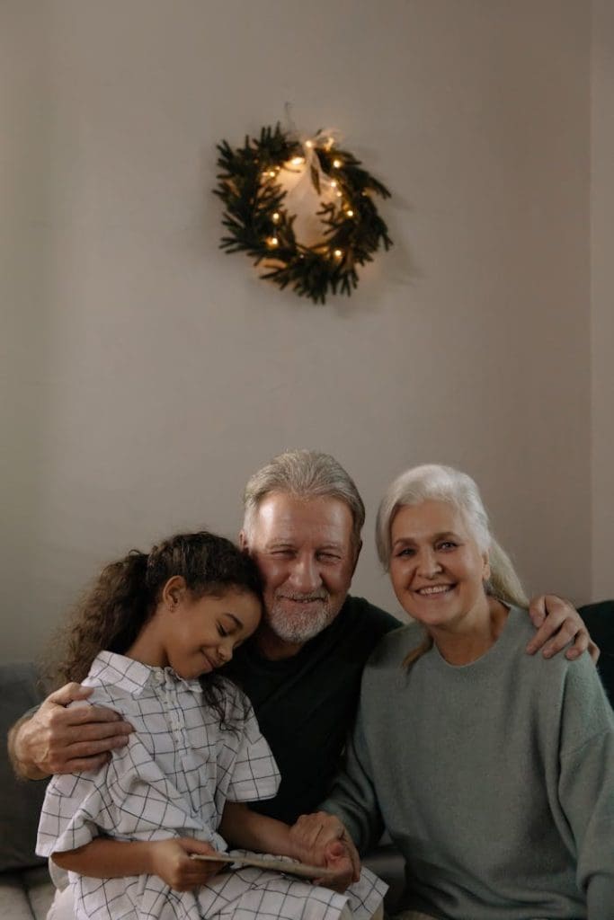 Grandparents and granddaughter hugging with a festive wreath in the background
